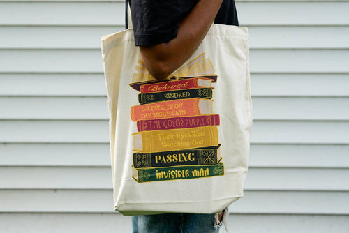 Tote bag with book stack design held by a person against a gray background